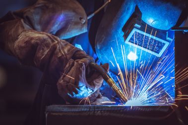 A welder is welding a FLANGE onto a piece of metal.